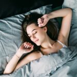 Young beautiful woman waking up in her bed fully rested. Woman stretching in bed after wake up. Healthy lifestyle. Wellness concept