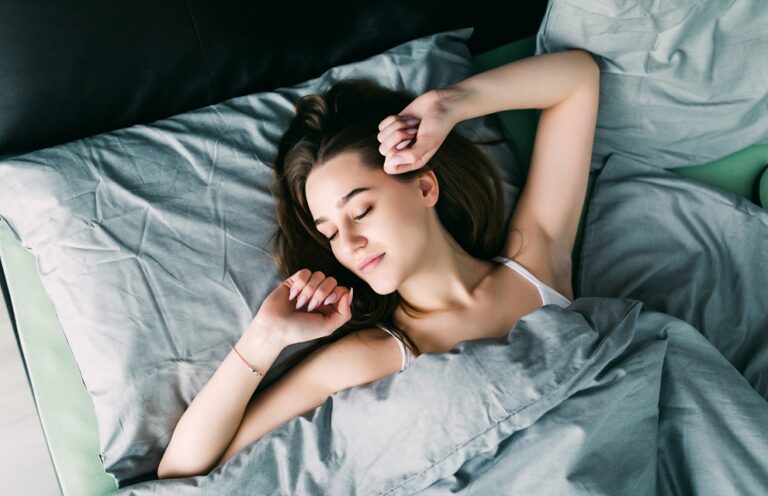 Young beautiful woman waking up in her bed fully rested. Woman stretching in bed after wake up. Healthy lifestyle. Wellness concept